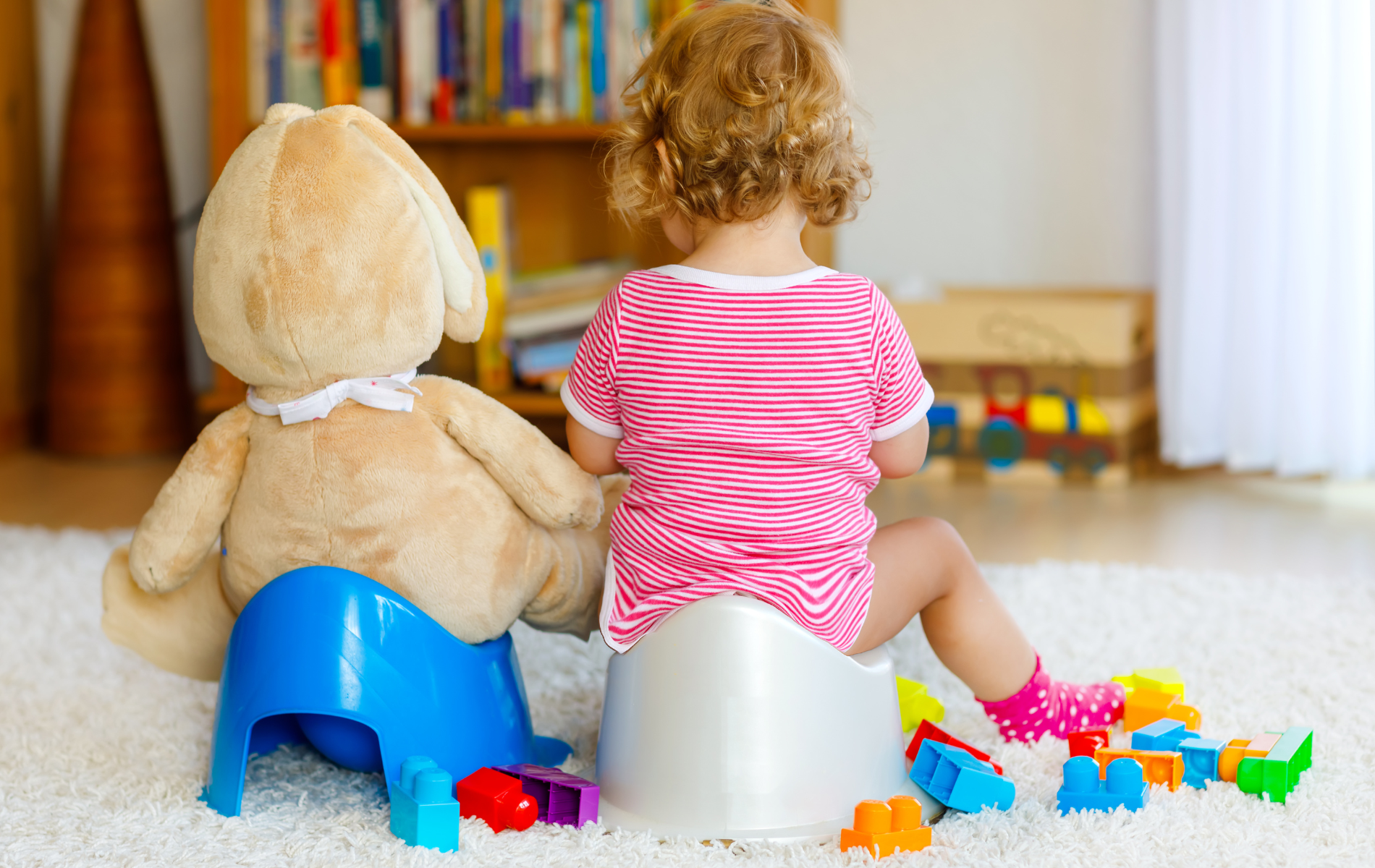 A little girl is sitting on a potty next to a teddy bear.