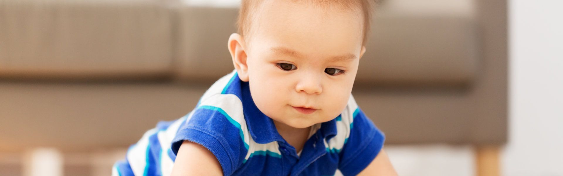 A baby in a blue shirt is crawling on the floor.