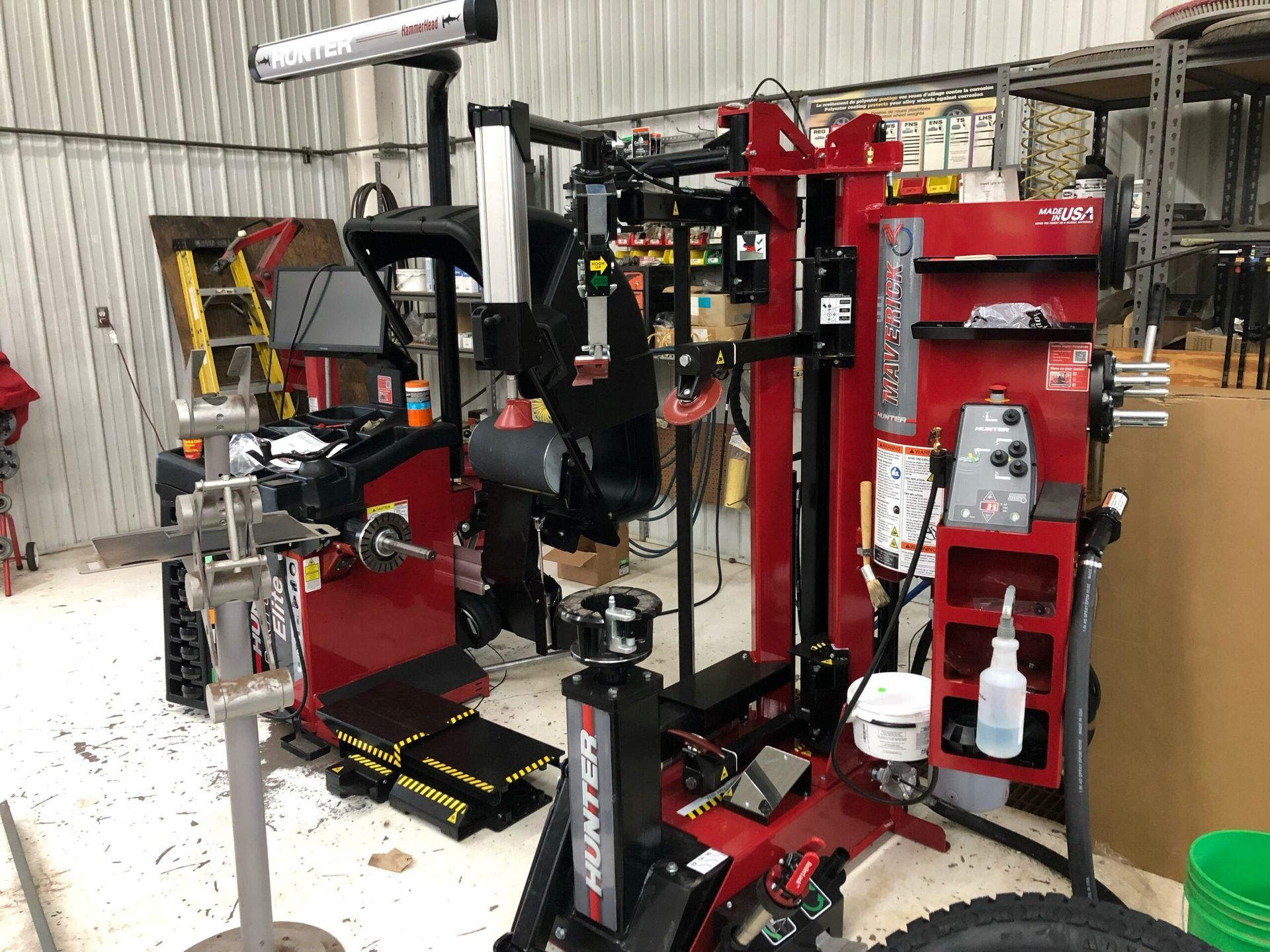 A tire changer is sitting in a garage next to a green bucket.