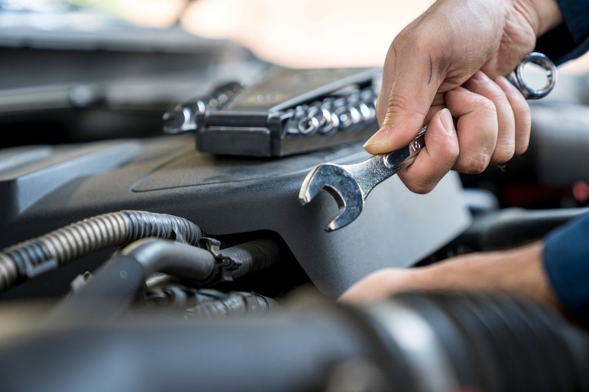 A person is working on a car engine with a wrench.