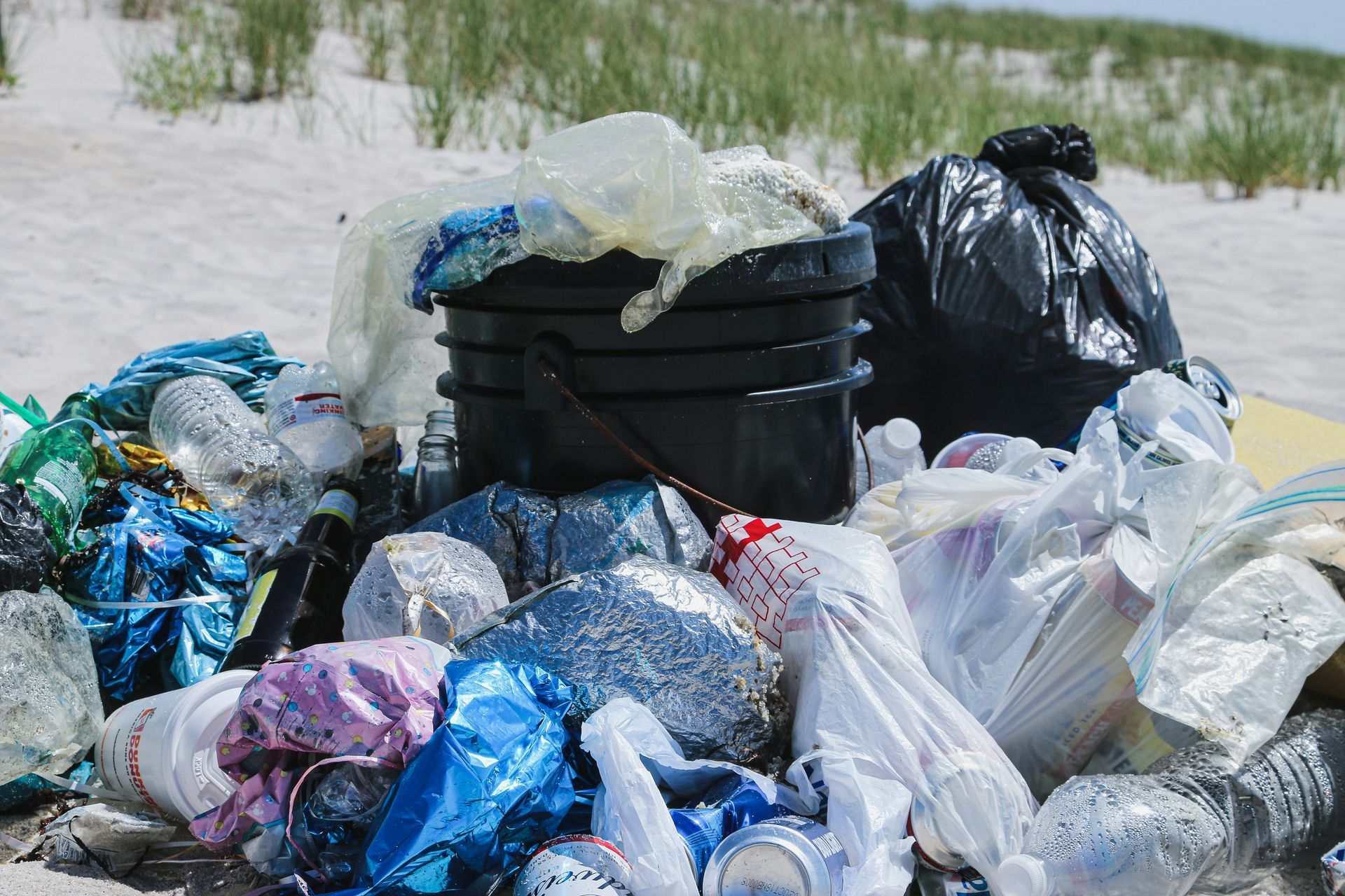 a pile of trash on the beach with a trash can in the middle .