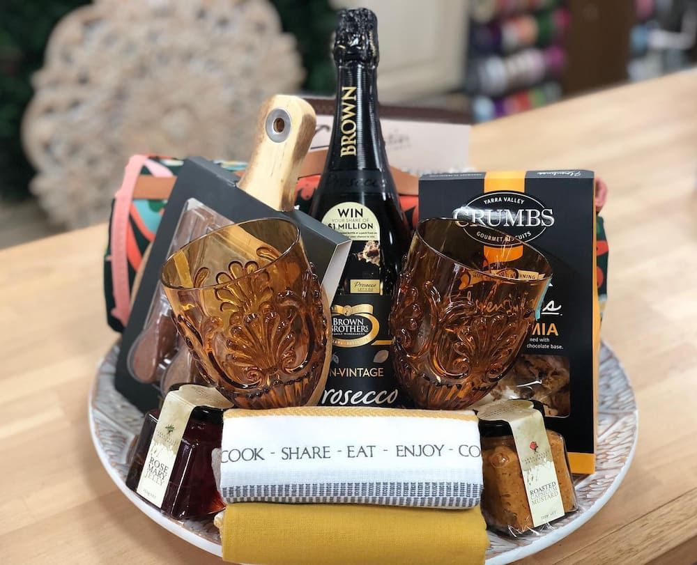 A Basket With A Bottle Of Wine, Glasses, Chocolates, And Cheese On A Table — Clover Country Flowers and Gifts In Pittsworth, QLD