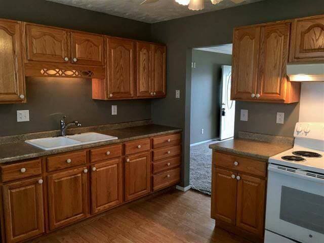 Kitchen with brown cabinets, gray walls, light countertops, white sink and stove, wooden floor.