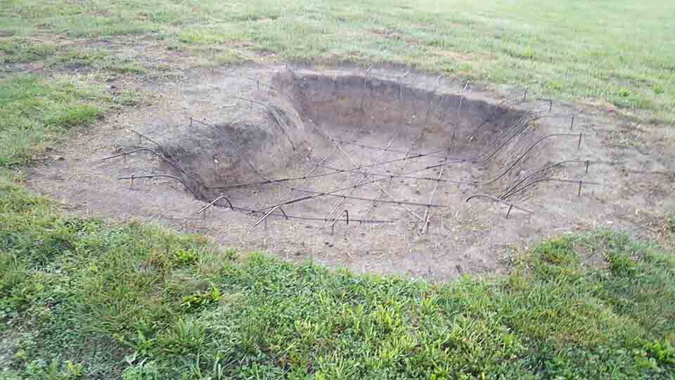 Crater-shaped depression in a grassy field, earth-toned with visible cracks.