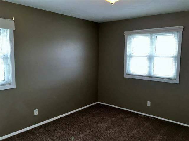 Empty bedroom with brown walls, two windows with white trim, and brown carpet.