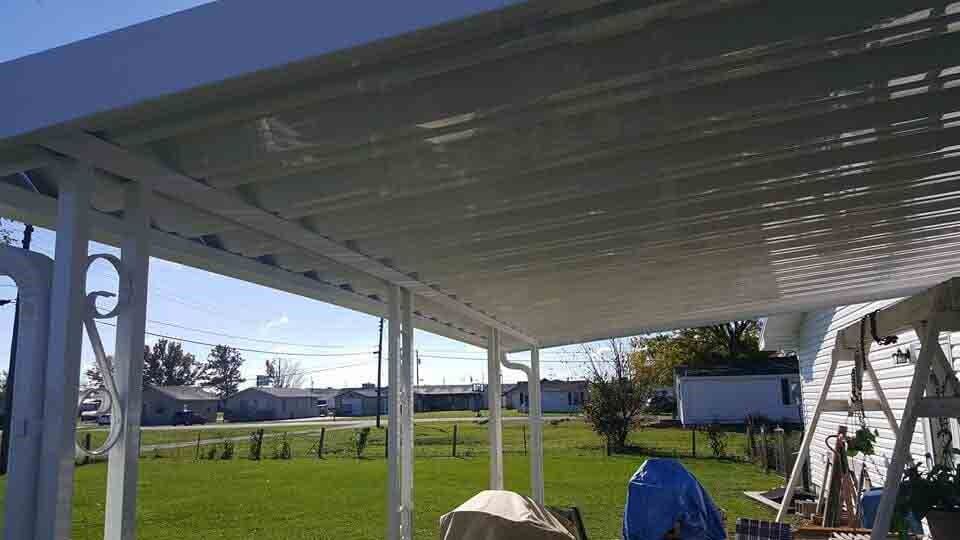 White-framed patio cover over a lawn, houses in the background on a sunny day.