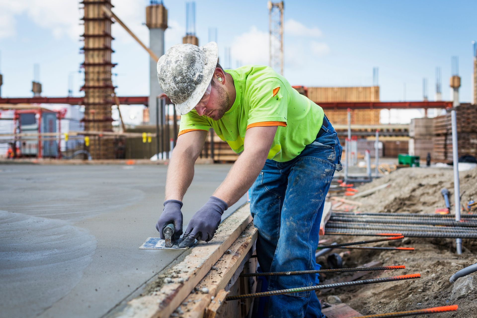A worker smoothing concrete at a construction site with buildings behind.