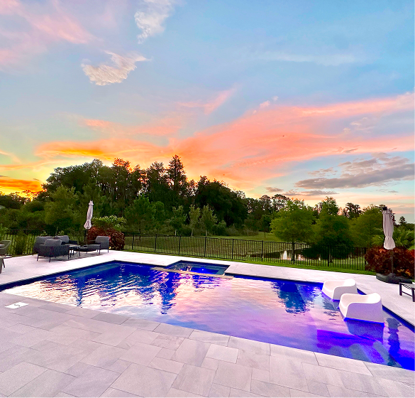 Swimming pool with vibrant sunset sky and trees in the background.