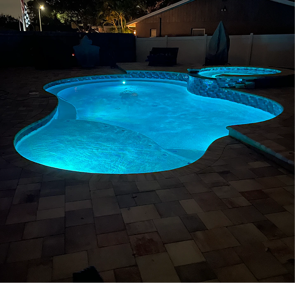A glowing blue swimming pool at night, surrounded by a brick patio.