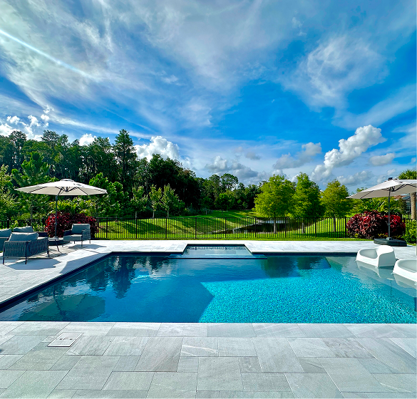 Pool with blue water and surrounding patio under a blue sky with clouds.