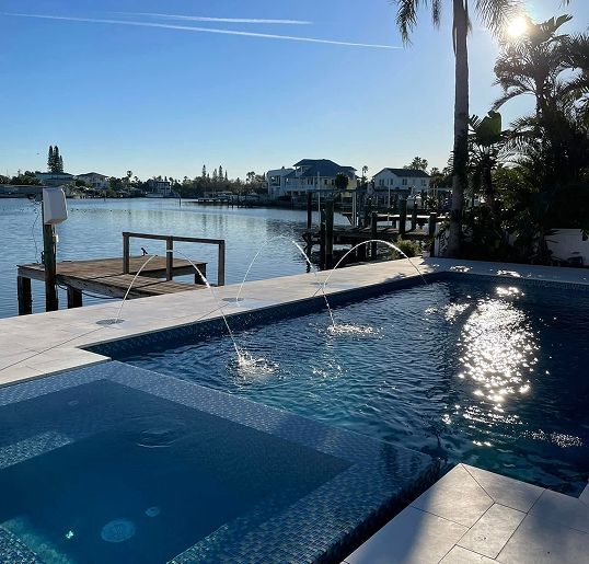 Poolside view with turquoise water, dock, palms, and a person sunbathing.