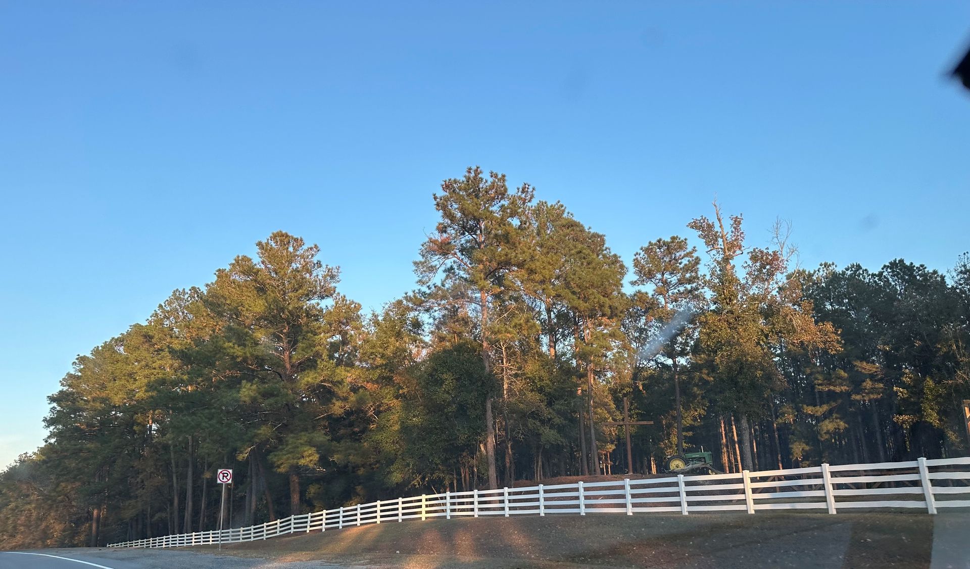 Trees behind a white picket fence under a blue sky.