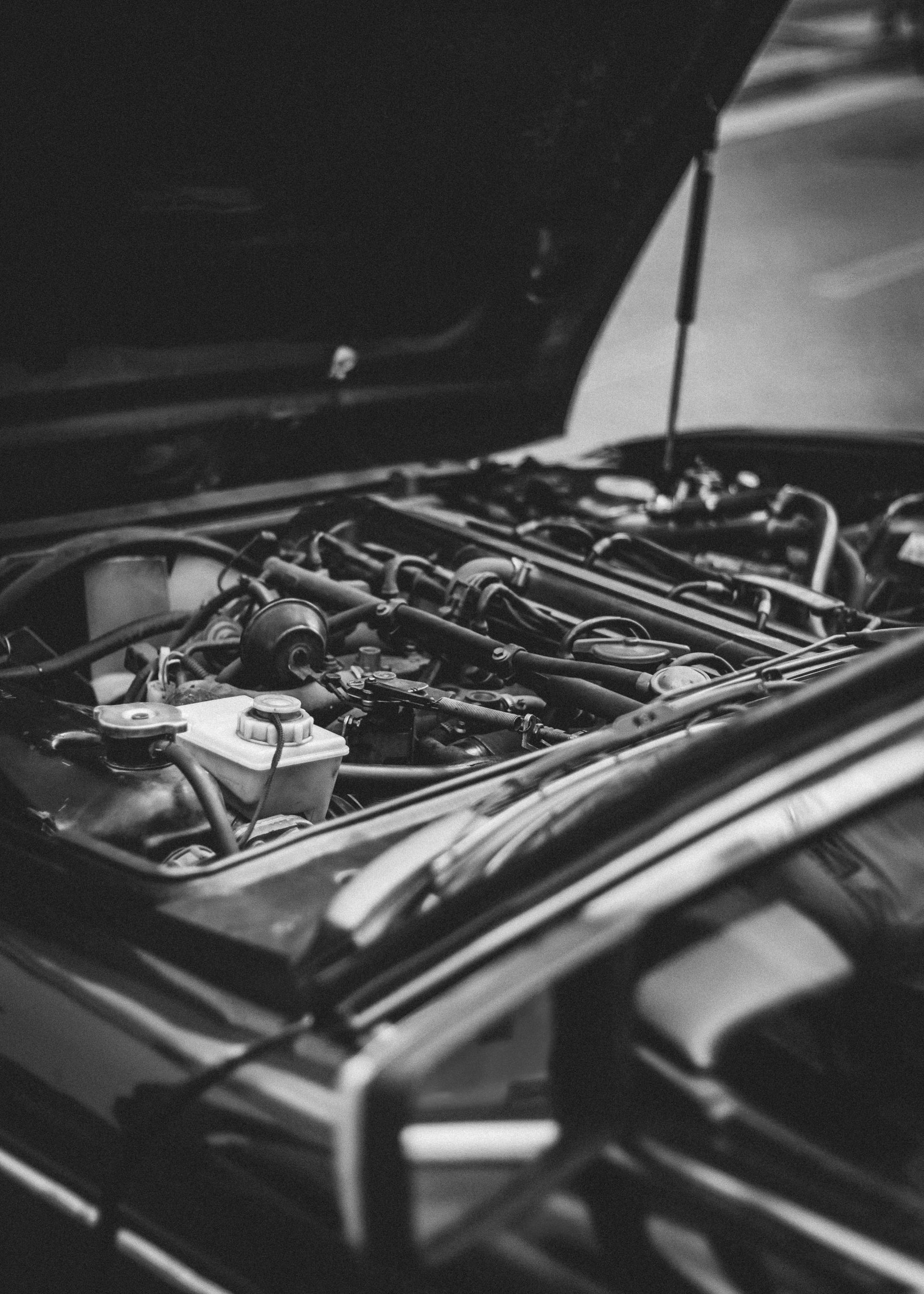 A black and white photo of a man working on a car engine.