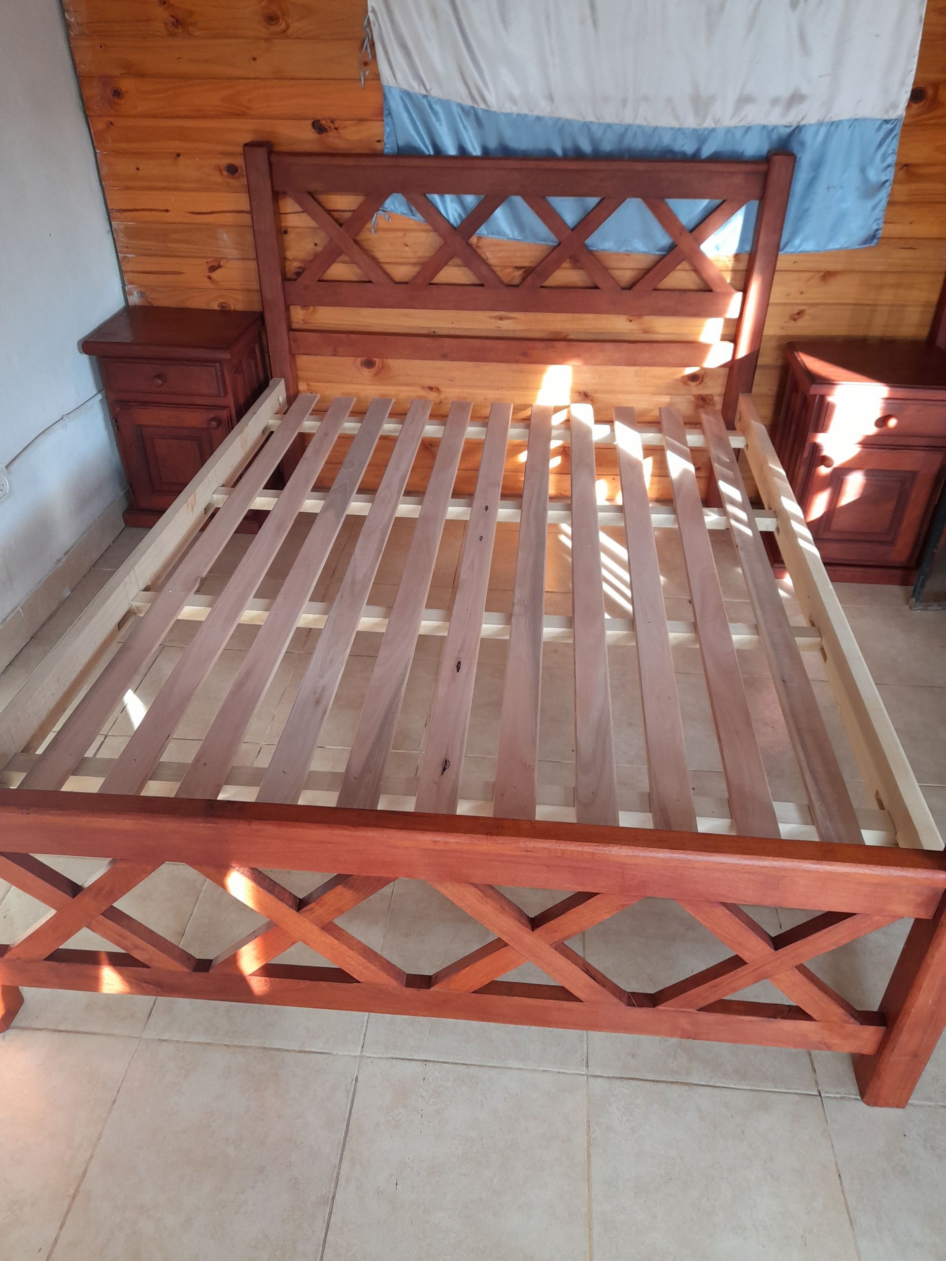 Estructura de cama de madera con diseño en forma de X en cabecera y pie de cama, cama vacía.