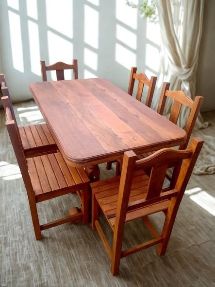 Mesa de comedor de madera y seis sillas, de color marrón, ubicadas en una habitación con entrada de luz.