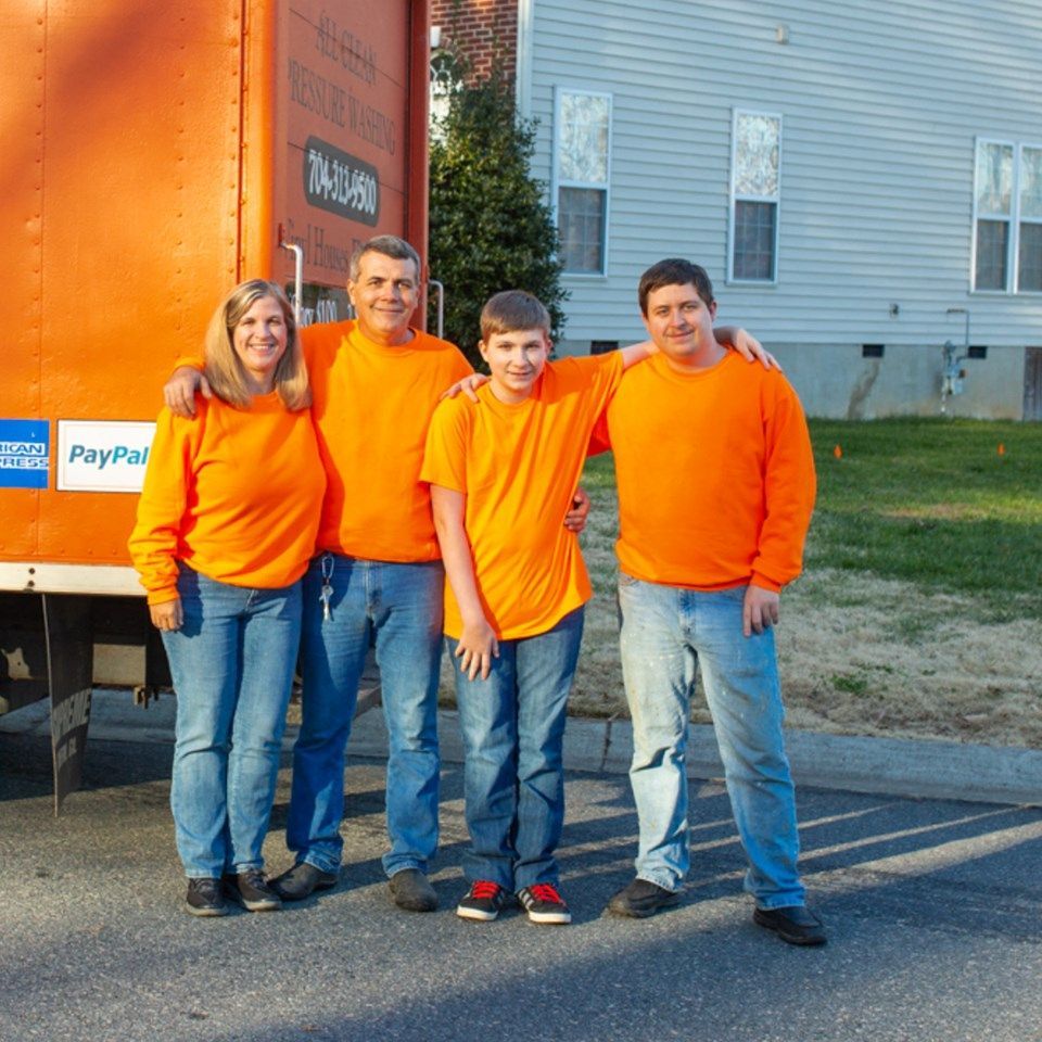 Four people in matching orange long-sleeved shirts and blue jeans stand together outdoors next to an orange trailer.