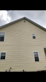 A view of the side of a two-story beige house with four windows and a small circular gable vent under the roof peak.