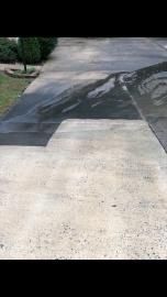 A concrete driveway with a stark, dark-stained patch contrasting against the lighter, weathered surface.