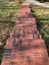A set of red brick outdoor steps leading down a grassy slope toward a concrete path.