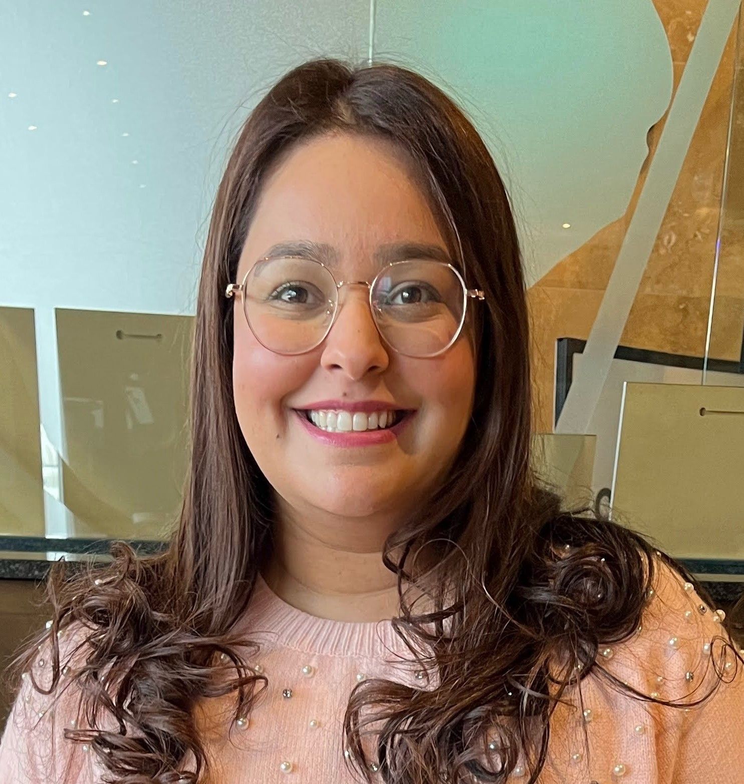 A woman wearing glasses and a pink sweater is smiling for the camera.