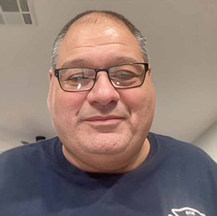 A man wearing glasses and a blue shirt is smiling for the camera.