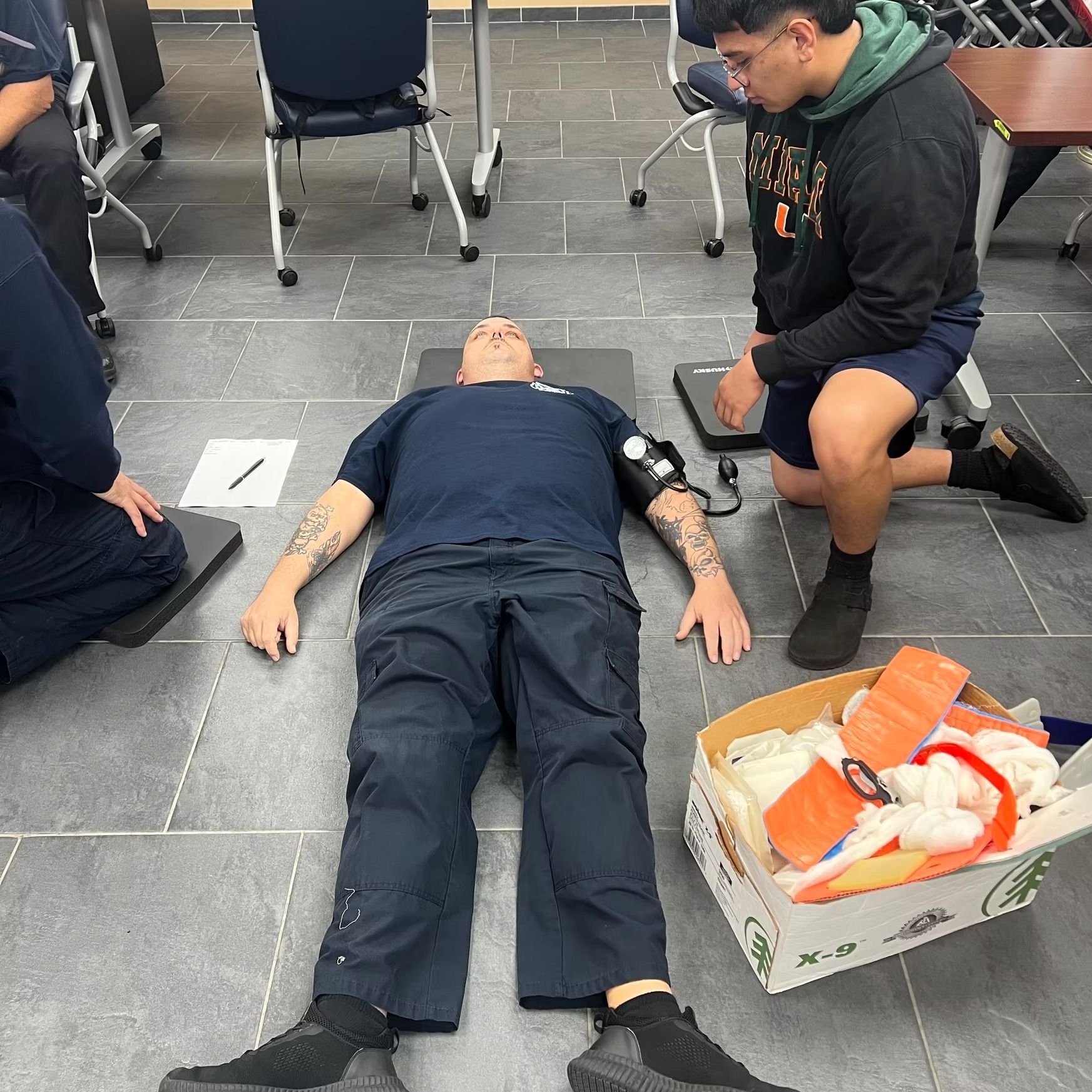 A man is laying on the floor next to a box of supplies.
