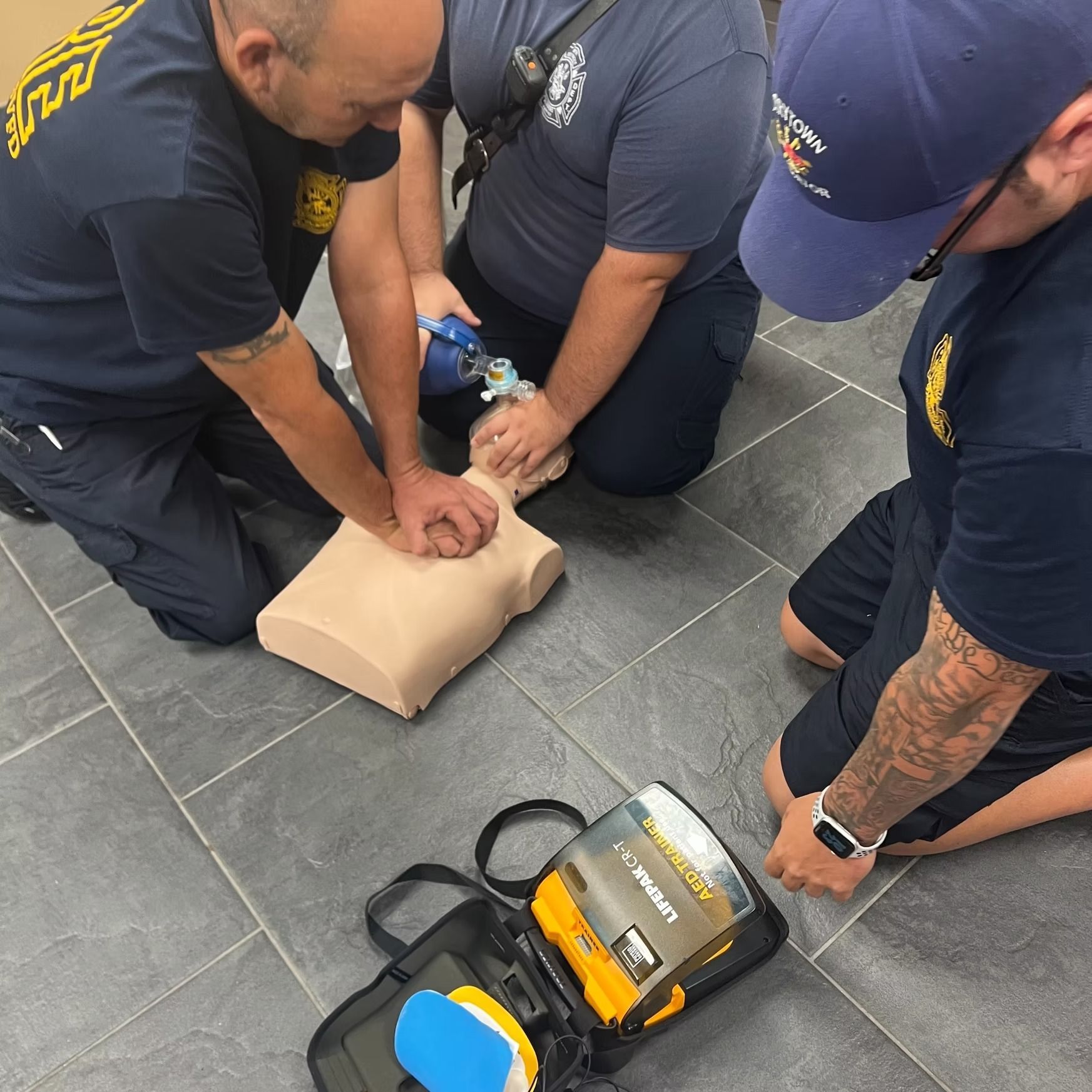 A group of men are practicing a defibrillator on a mannequin