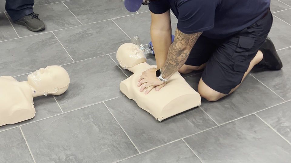 A man is kneeling on the floor doing a heart massage on a mannequin.