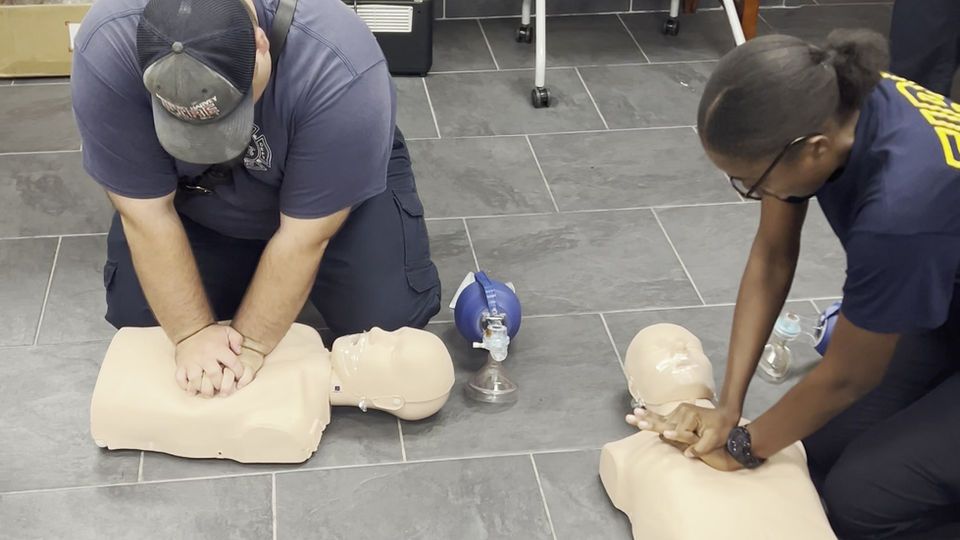 A man and a woman are practicing on a mannequin.
