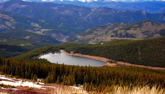 There is a lake in the middle of a forest in the mountains.