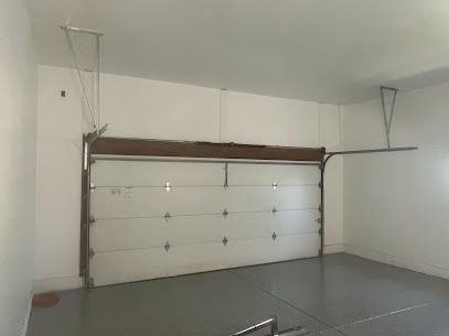 An empty garage with a white garage door and a gray floor.