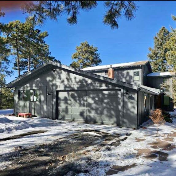 A house with a garage is surrounded by snow and trees.