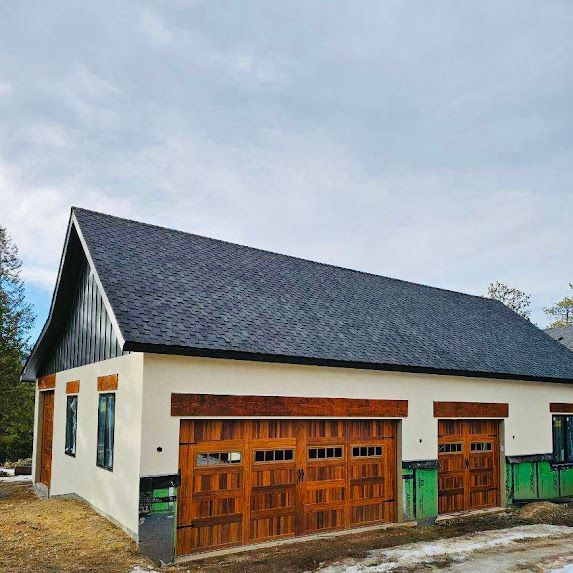 A white house with a black roof and wooden garage doors.