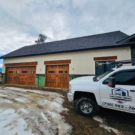 A white truck is parked in front of a house with wooden garage doors.