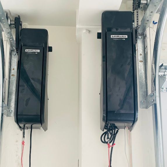 Two black garage door openers are mounted on a white wall.