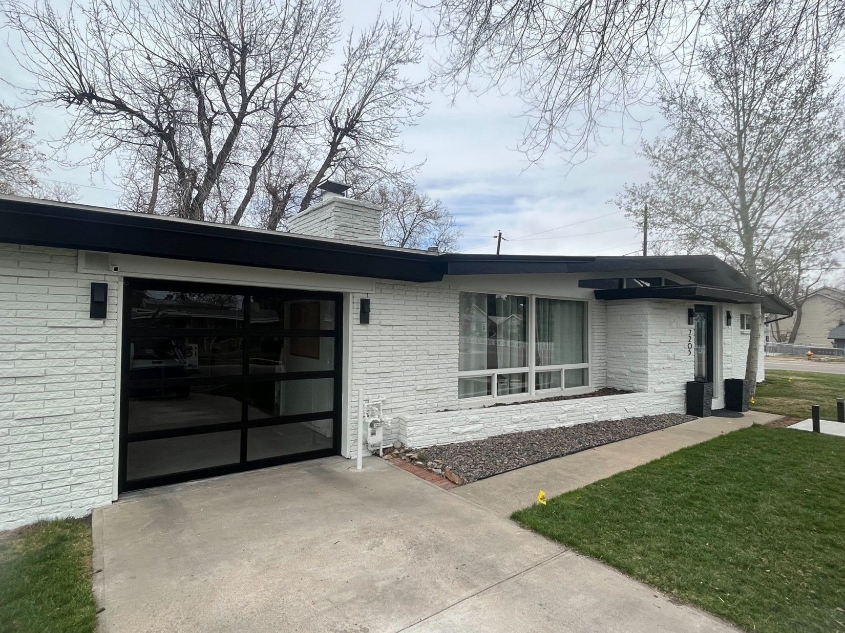 A white brick house with a black roof and a black garage door.