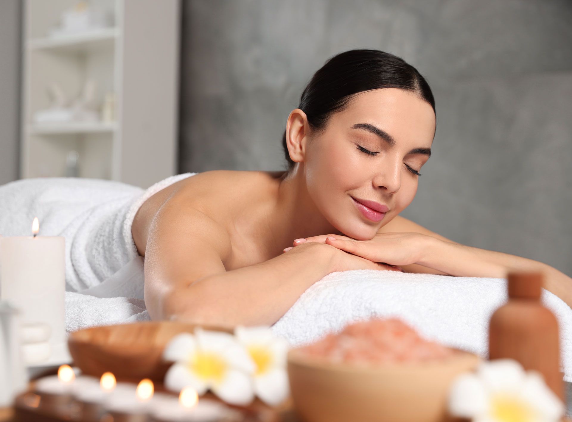 A woman is laying on a massage table in a spa with her eyes closed