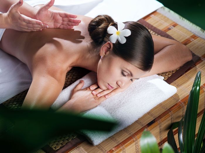 Woman receiving back massage at a spa; flower in hair.