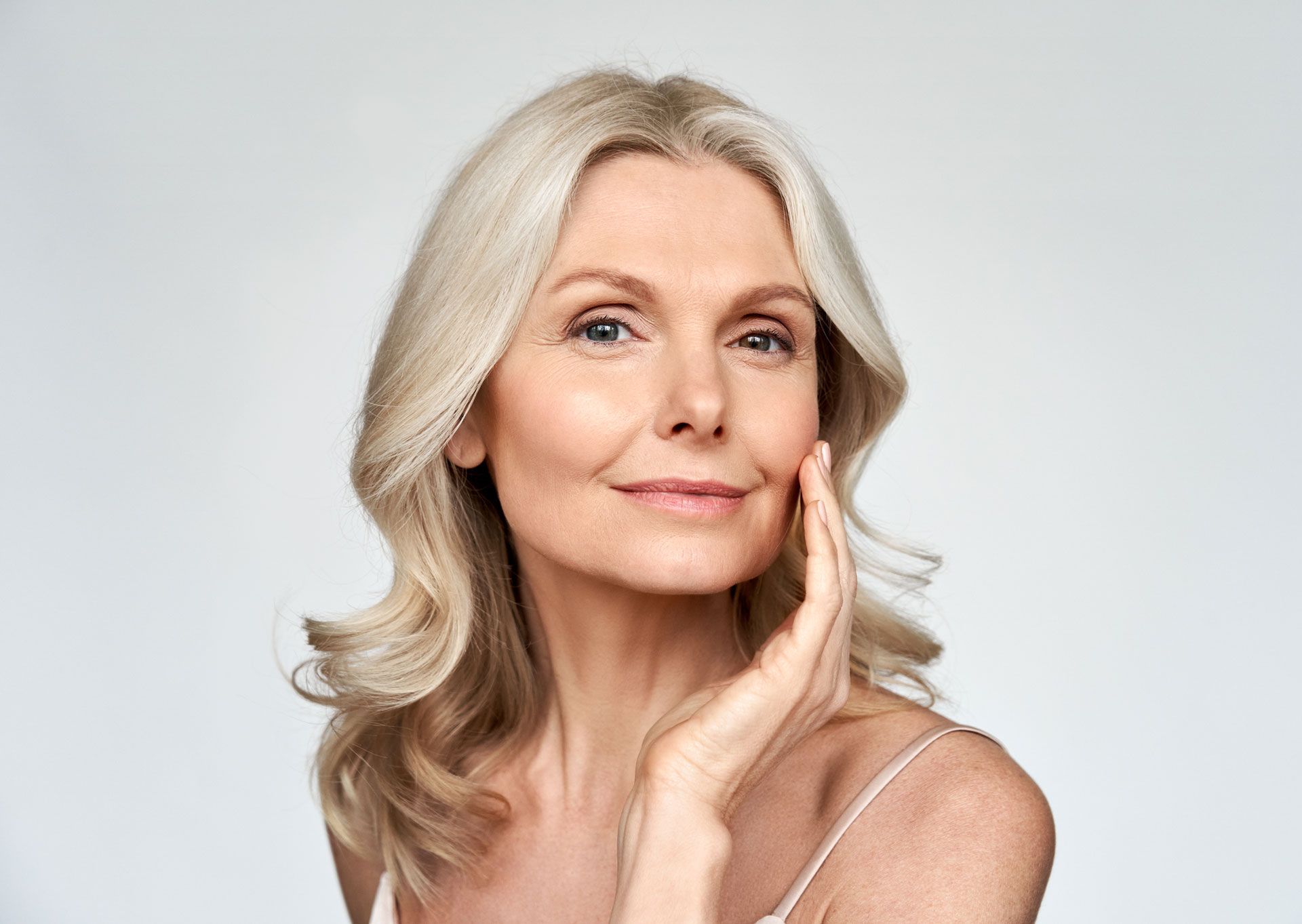 A woman is touching her face with her hand and smiling.