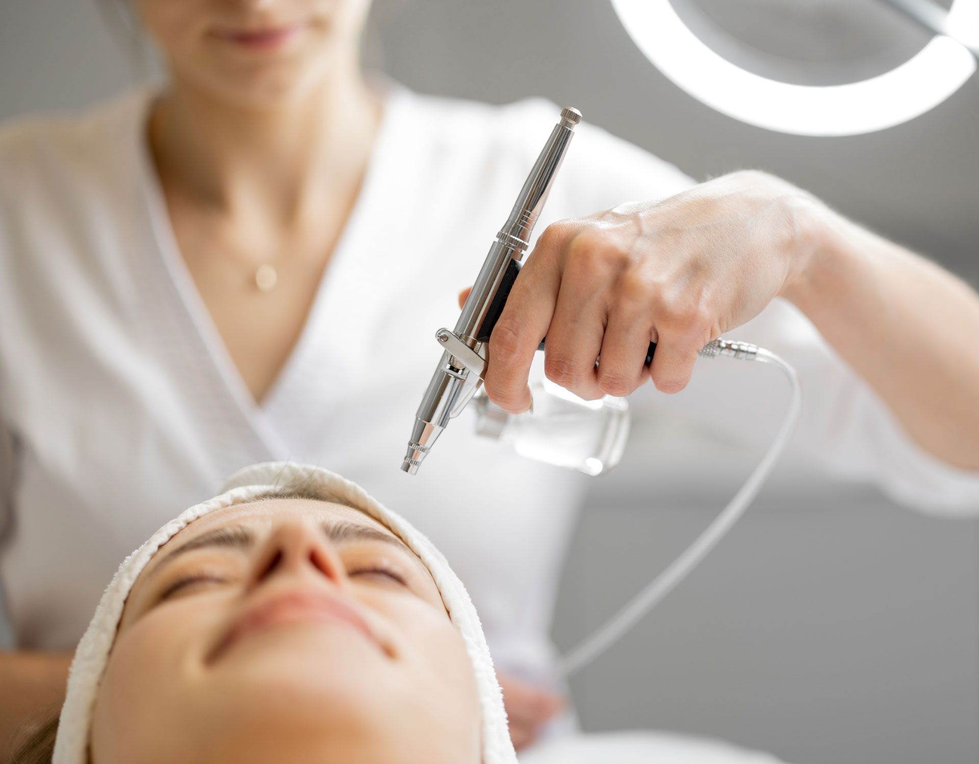 A woman is getting an airbrush treatment on her face.