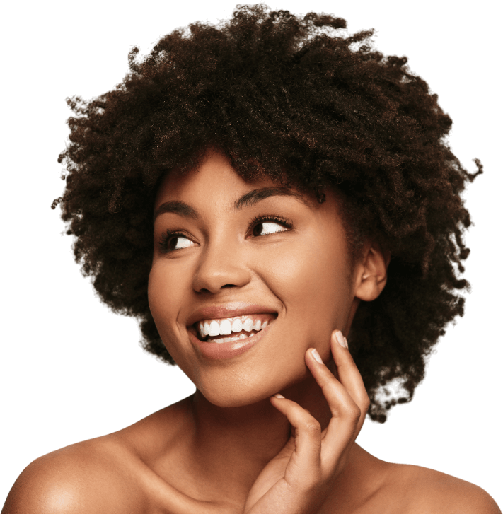 A woman with curly hair is smiling and touching her face