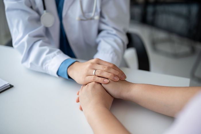 Doctor comforting patient by holding their hands at a white desk.