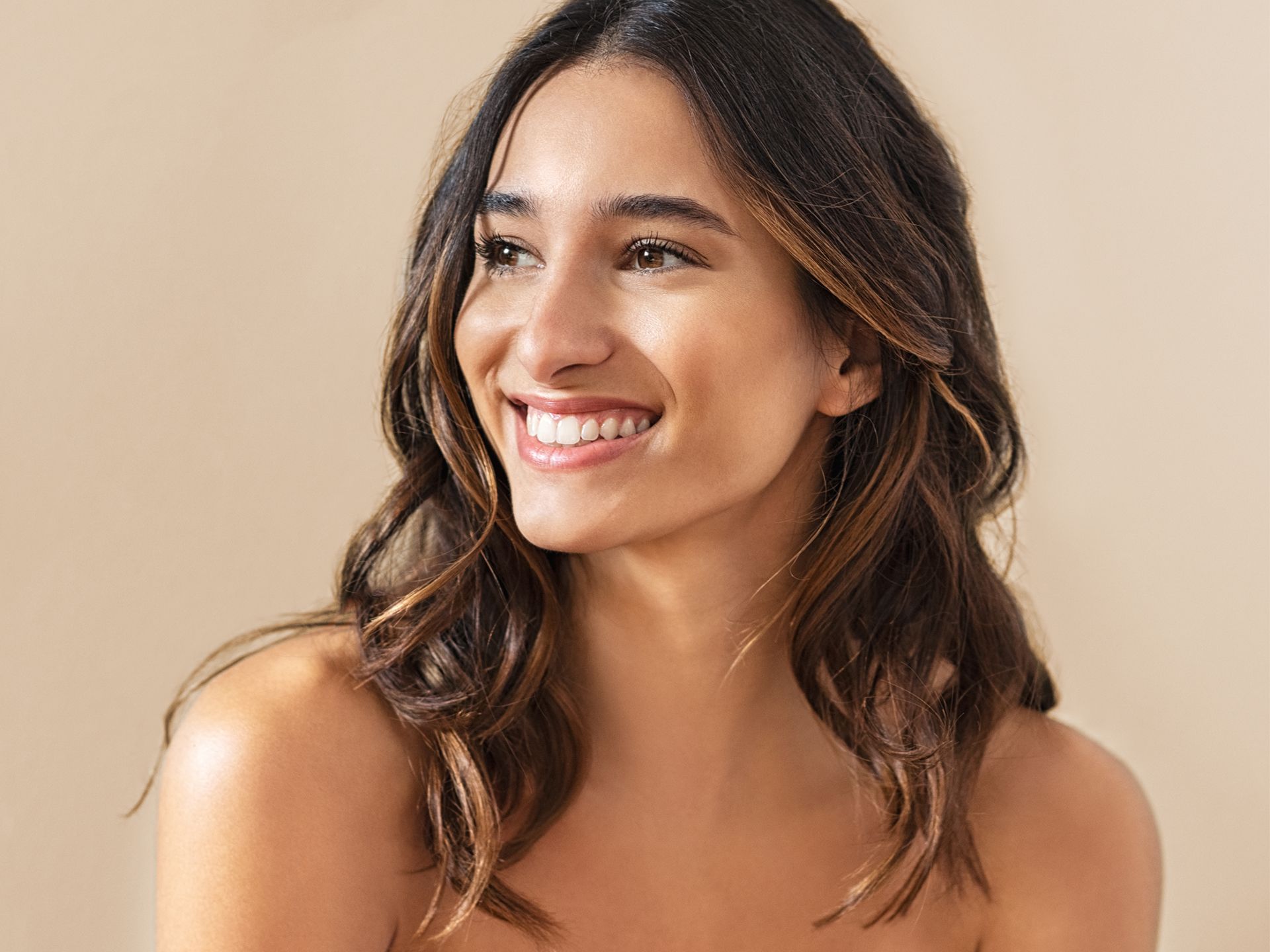 A woman with long hair is smiling and looking to the side.