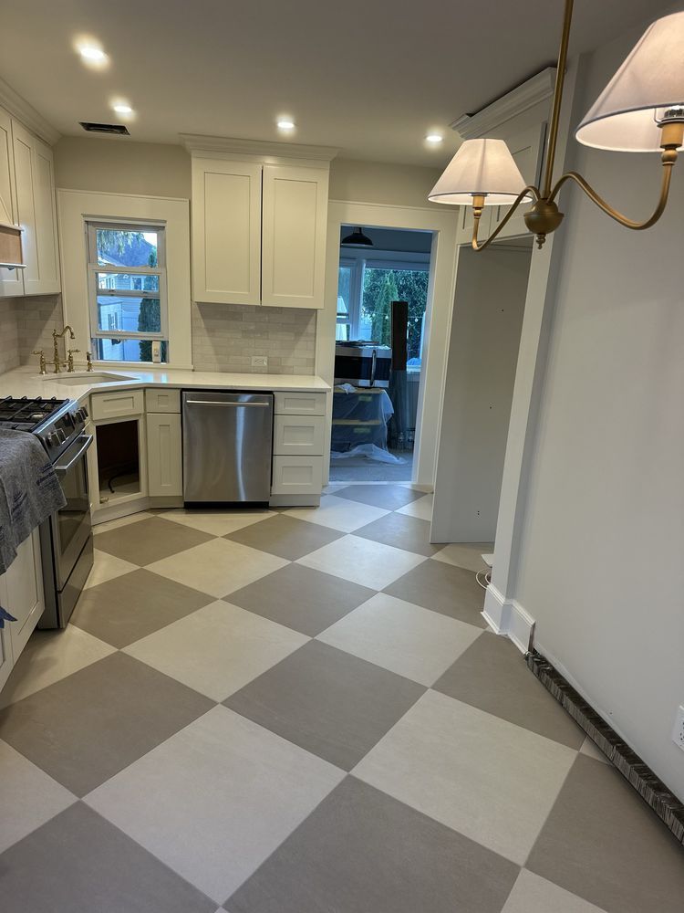 A kitchen with white cabinets, stainless steel appliances, and a gray and white checkered floor, viewed from a dining area.