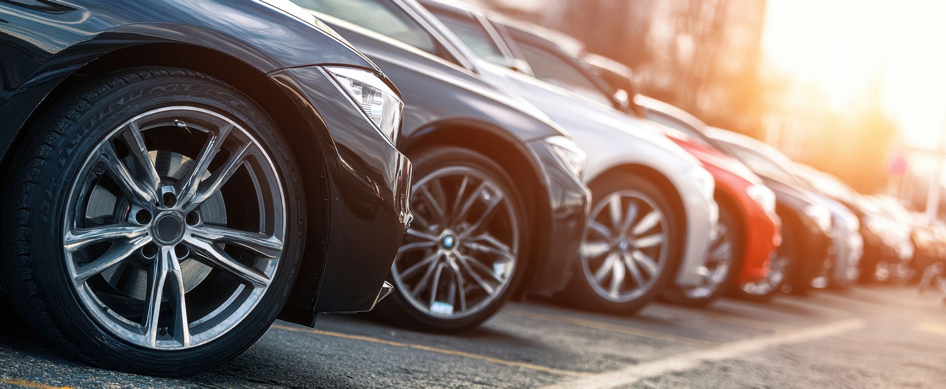 A row of parked cars shown in a close-up, low-angle view with the sun setting in the background.