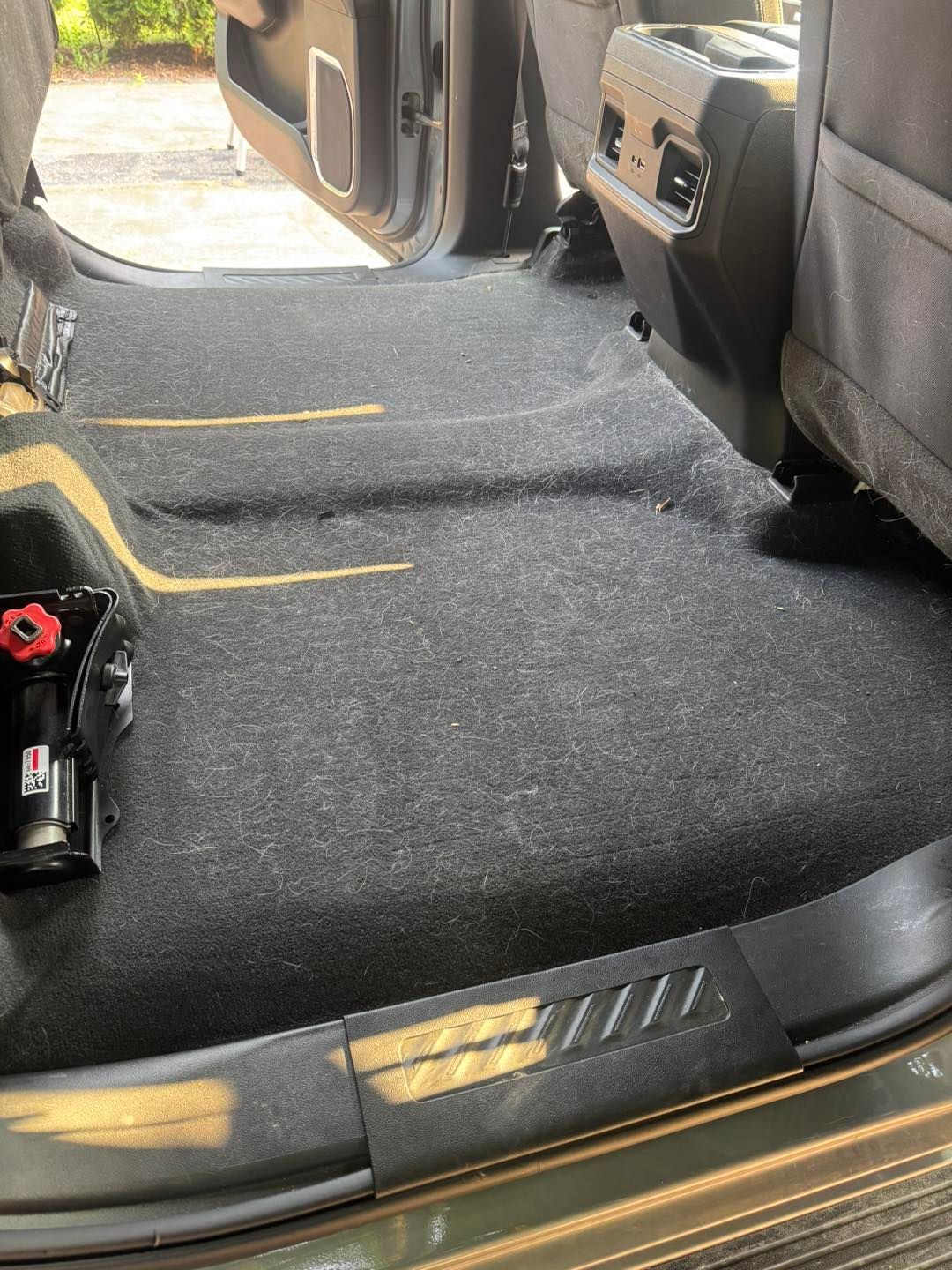 Gray carpeted floor of a truck’s backseat area with a vehicle jack and yellow tape on the trim and floor.