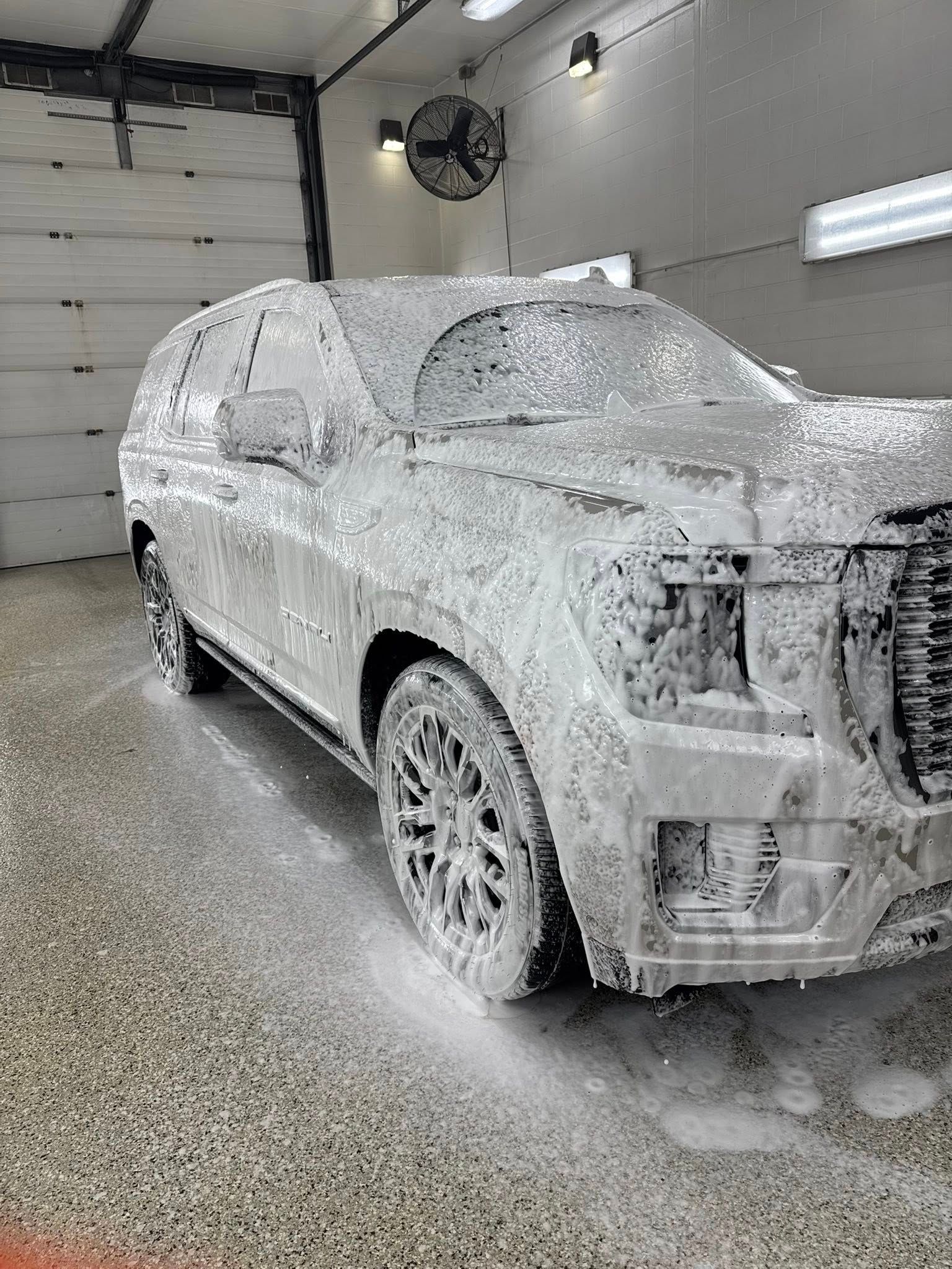 A side view of an SUV in a garage, completely covered in thick white car wash soap foam.