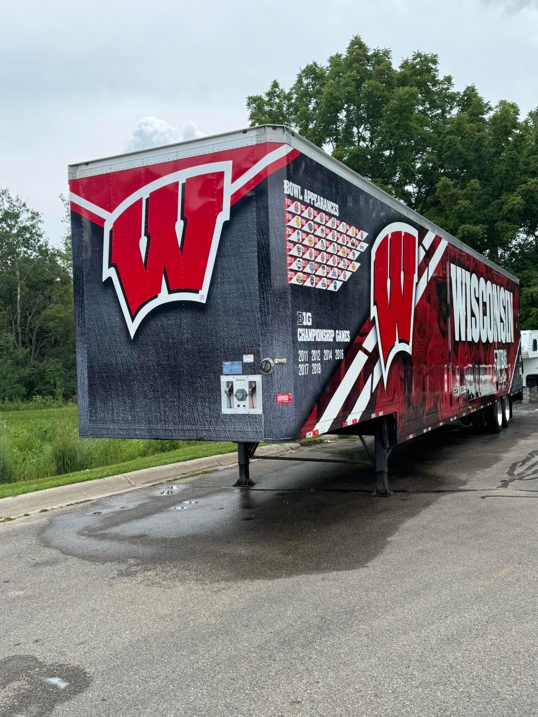 A semi-trailer wrapped in Wisconsin Badgers branding, featuring the red 'W' logo and team name on a black background.