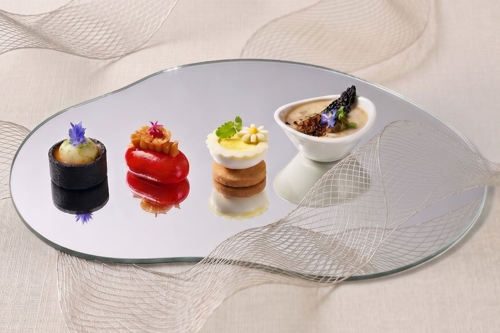 Four elegant mini desserts on a mirrored platter, each with distinct colorful toppings.
