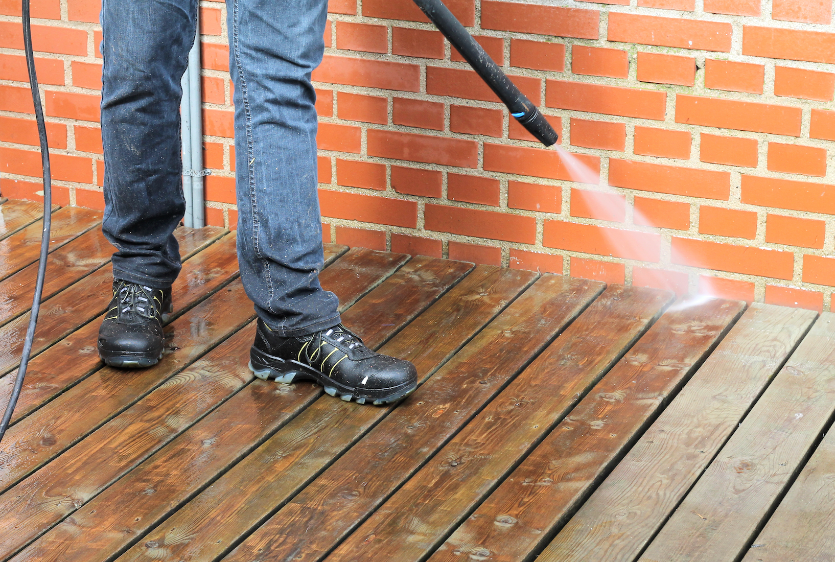 A man is cleaning a wooden deck with a high pressure washer.